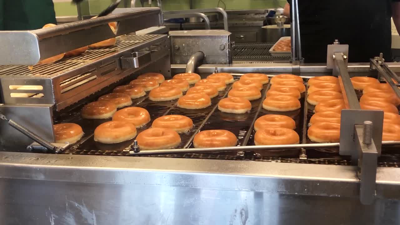 A quality control baker removing the imperfect doughnuts from a deep fat fryer