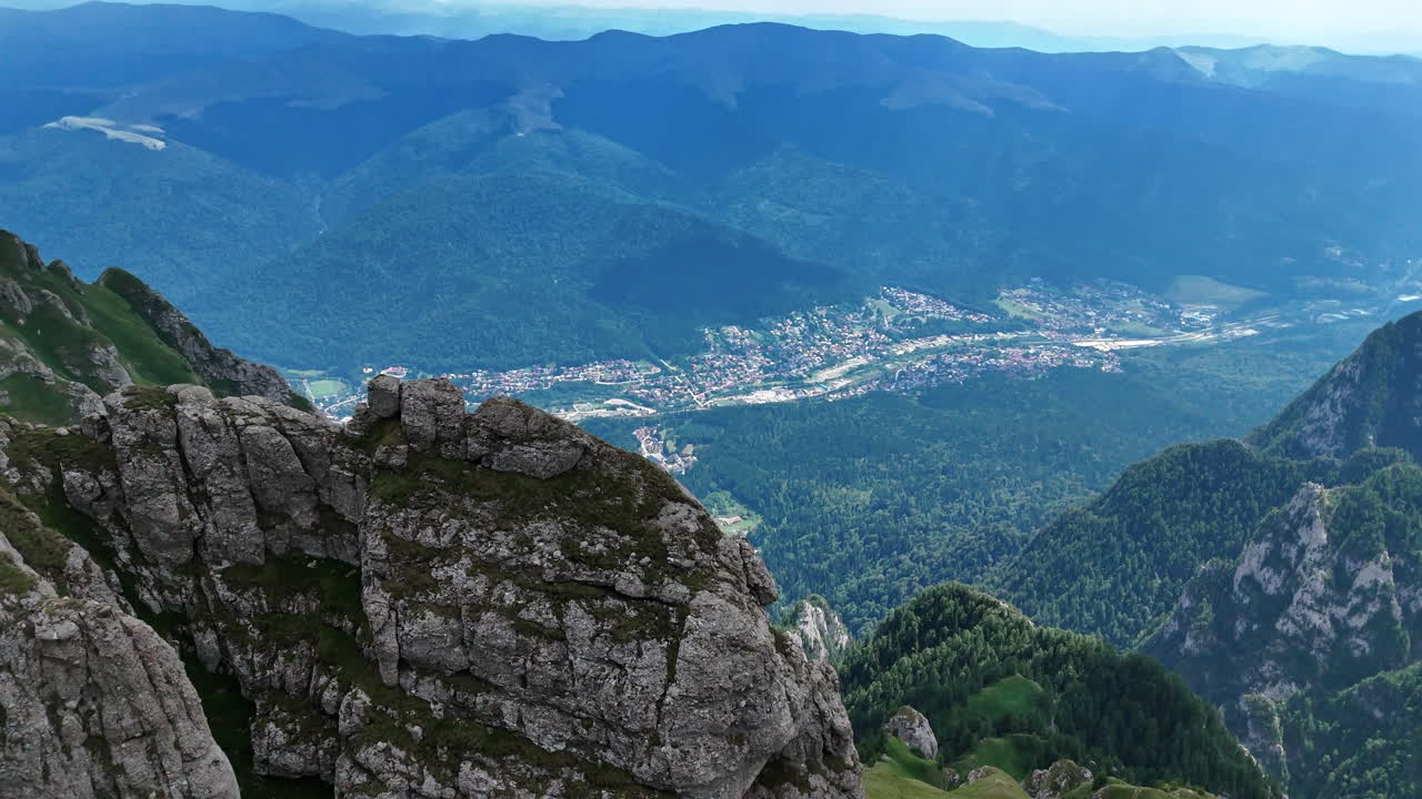 Úchvatné Jižní Karpaty se šedými holými vrcholy skal. Letecký pohled na krásné město v zeleném údolí mezi horami. Rumunsko