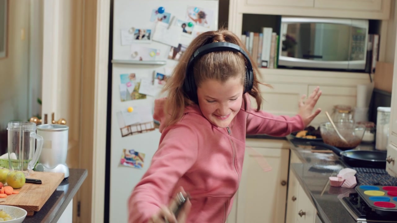 Happy Young Girl Dancing and Listening to Music in Kitchen
