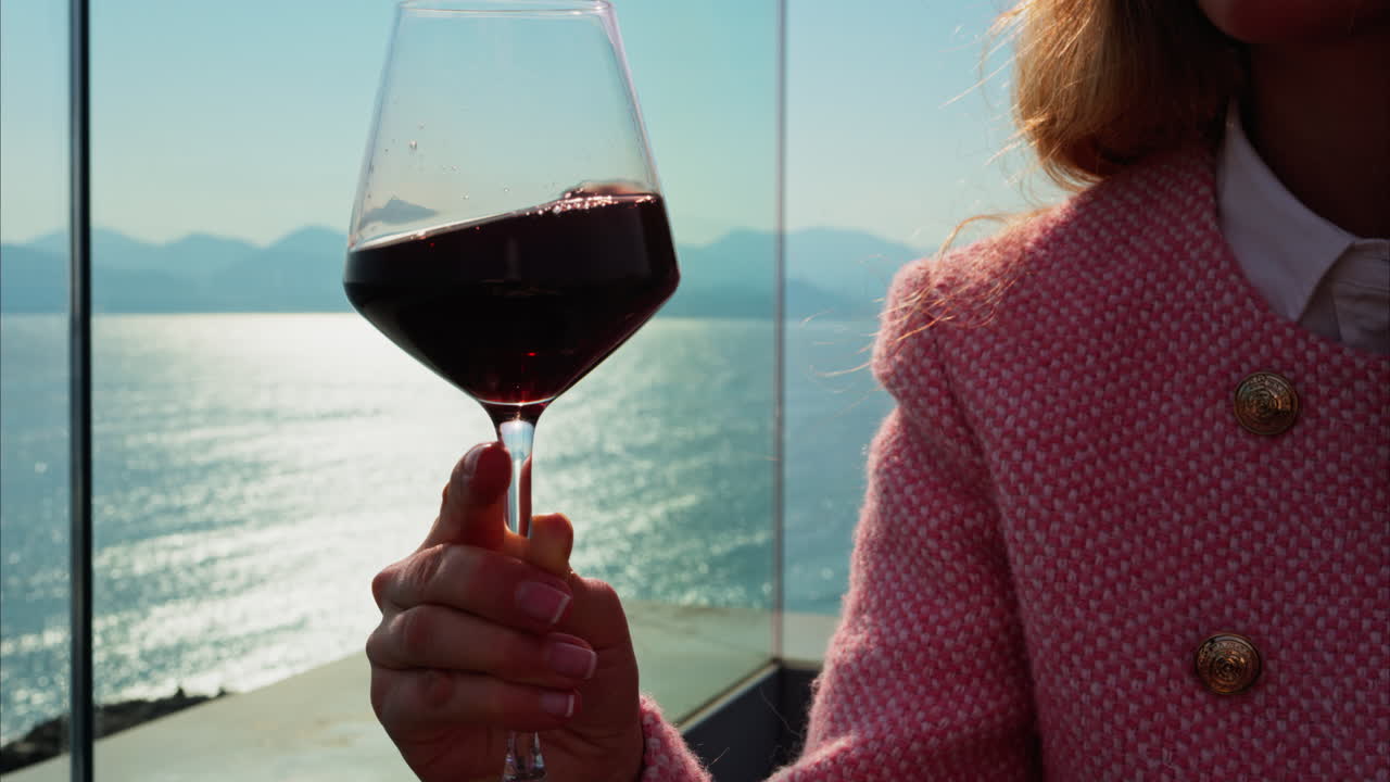 Close up of a woman swirling a glass of red wine on a table at a terrace with a sea view
