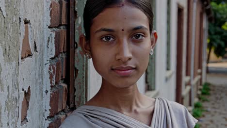 serene young student wearing traditional sari, standing near weathered wall, embodying quiet confidence and cultural resilience with natural, contemplative presence