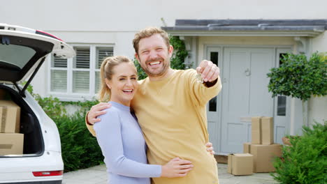 portrait of couple holding keys outside new home on moving day unloading boxes from car