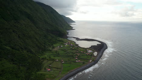 Erstaunliche-Luftaufnahme-Einer-Küstenlandschaft-Mit-Einem-Kleinen-Dorf-Und-Einem-Steilen-Hang,-Der-Sich-Aus-Dem-Meer-Erhebt