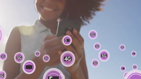 Animation-of-5g-purple-text-banners-over-african-american-woman-using-smartphone-outdoors