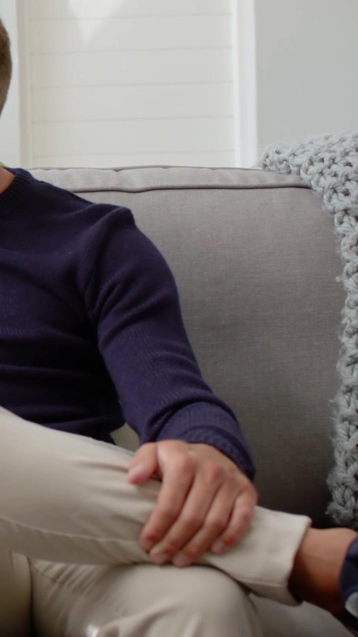 Vertikal video: Mand i marineblå strik taler med partner, kigger mens kamera panorerer på sofa, med plads til tekst.