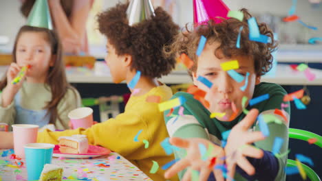 boy blowing confetti at camera at birthday party with friends and parents at home