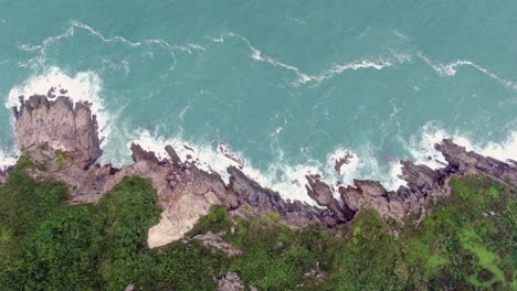 Aerial-view-of-a-jagged-rock-island,-surrounded-with-lush-green-nature-and-Hong-Kong-bay-water