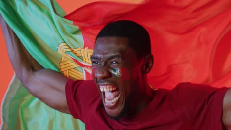 Happy-african-american-male-football-supporter-with-flag-of-portugal-over-pink-lighting