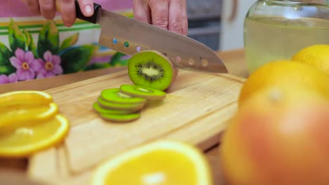 manos de mujeres amas de casa cortadas con un cuchillo kiwi fresco en la tabla de corte de la mesa de la cocina