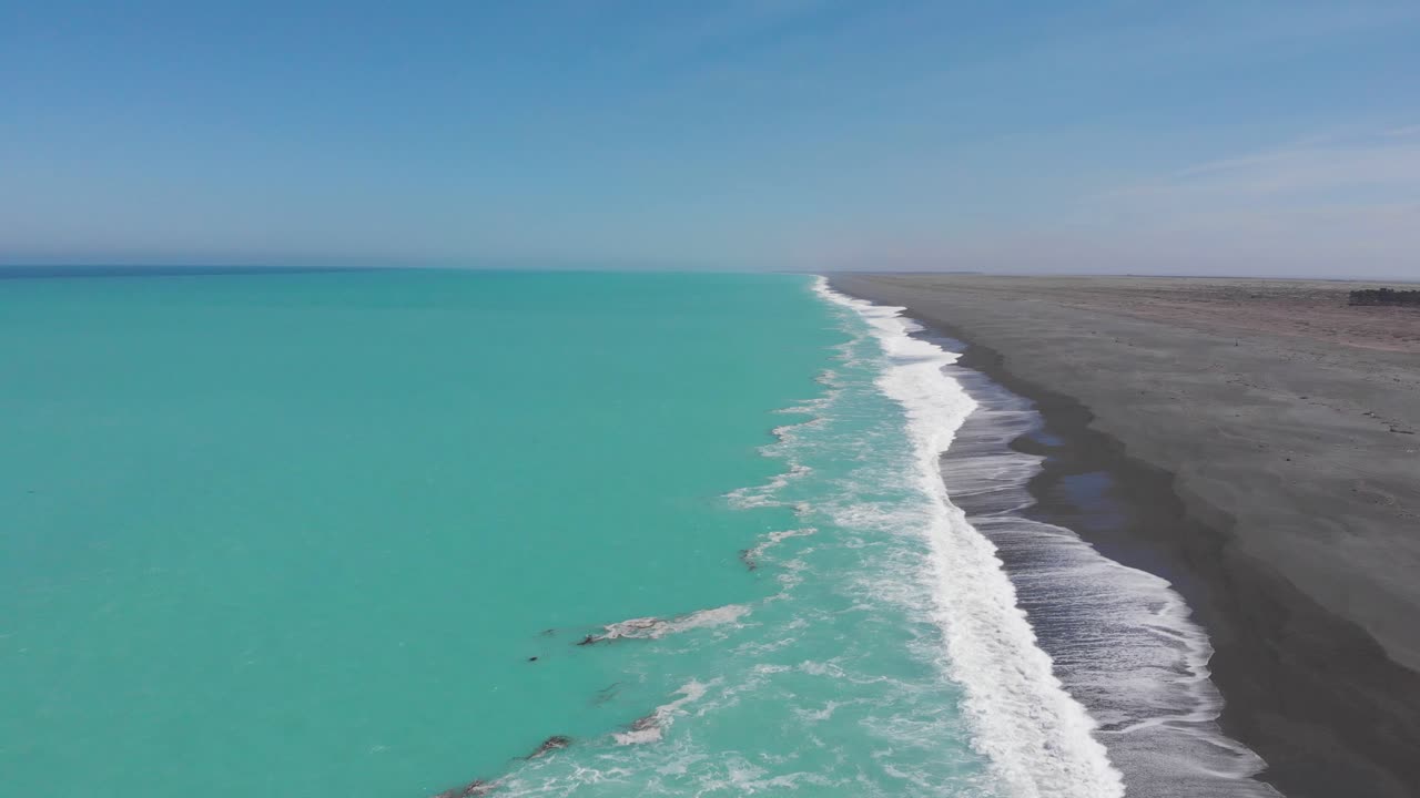 Scenic drone view of coastal line of New Zealand´s turquoise ocean and dark sand beach in 4k on a clear sunny day.