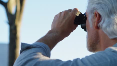 senior man looking through binoculars at countryside 4k