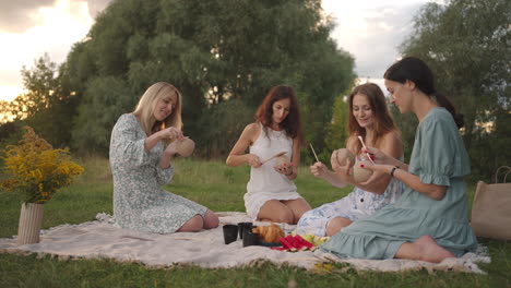 a group of young women concentrates on drawing patterns on clay products with the help of tools decorate molded objects talking smiling in a meadow in nature in an open space. general view