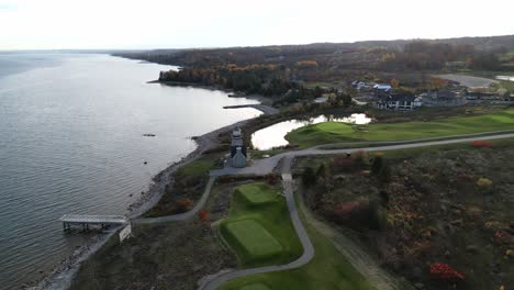 Drone-showing-a-golf-course-with-a-lighthouse-on-the-lakeshore-of-a-large-lake