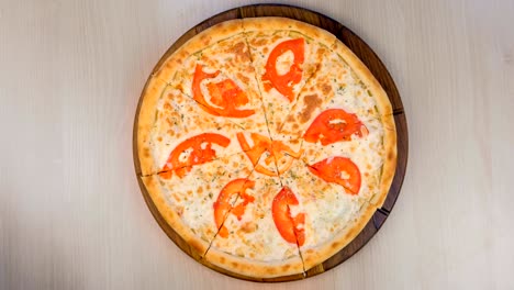 cortando pizza con tomates y queso en una tabla de madera.
