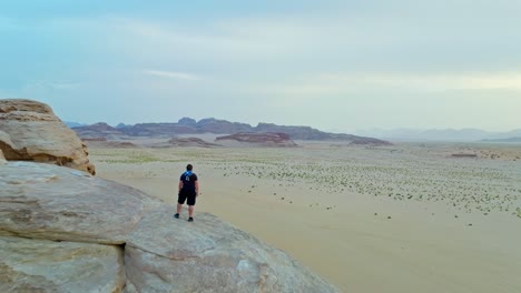 Hombre-De-Pie-En-Una-Formación-Rocosa-En-El-Desierto-De-Wadi-Rum,-Jordania---Retroceso-Aéreo