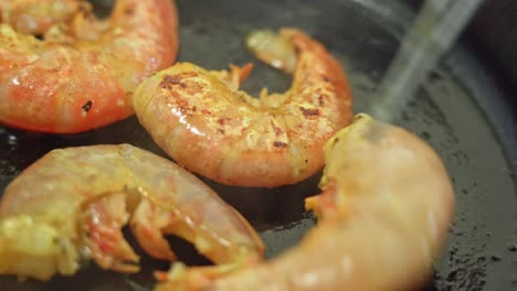 delicious shrimp fry in oily black metal pan, extreme close-up, flipped over