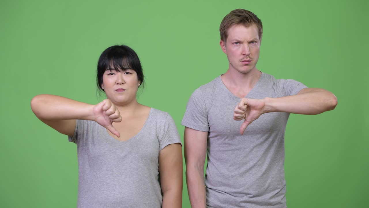 Young angry multi-ethnic couple giving thumbs down together