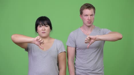 young angry multi-ethnic couple giving thumbs down together