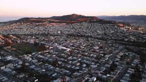 Daly-City-Alberga-Vistas-Aéreas-De-Drones-Con-La-Montaña-San-Bruno-En-El-Fondo-Durante-La-Puesta-De-Sol,-Cielo-Degradado