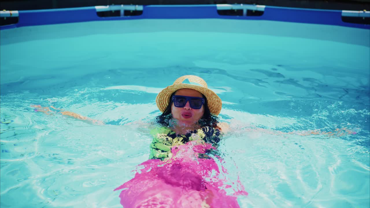 Woman relaxing in swimming pool wearing sunglasses and straw hat with colorful float