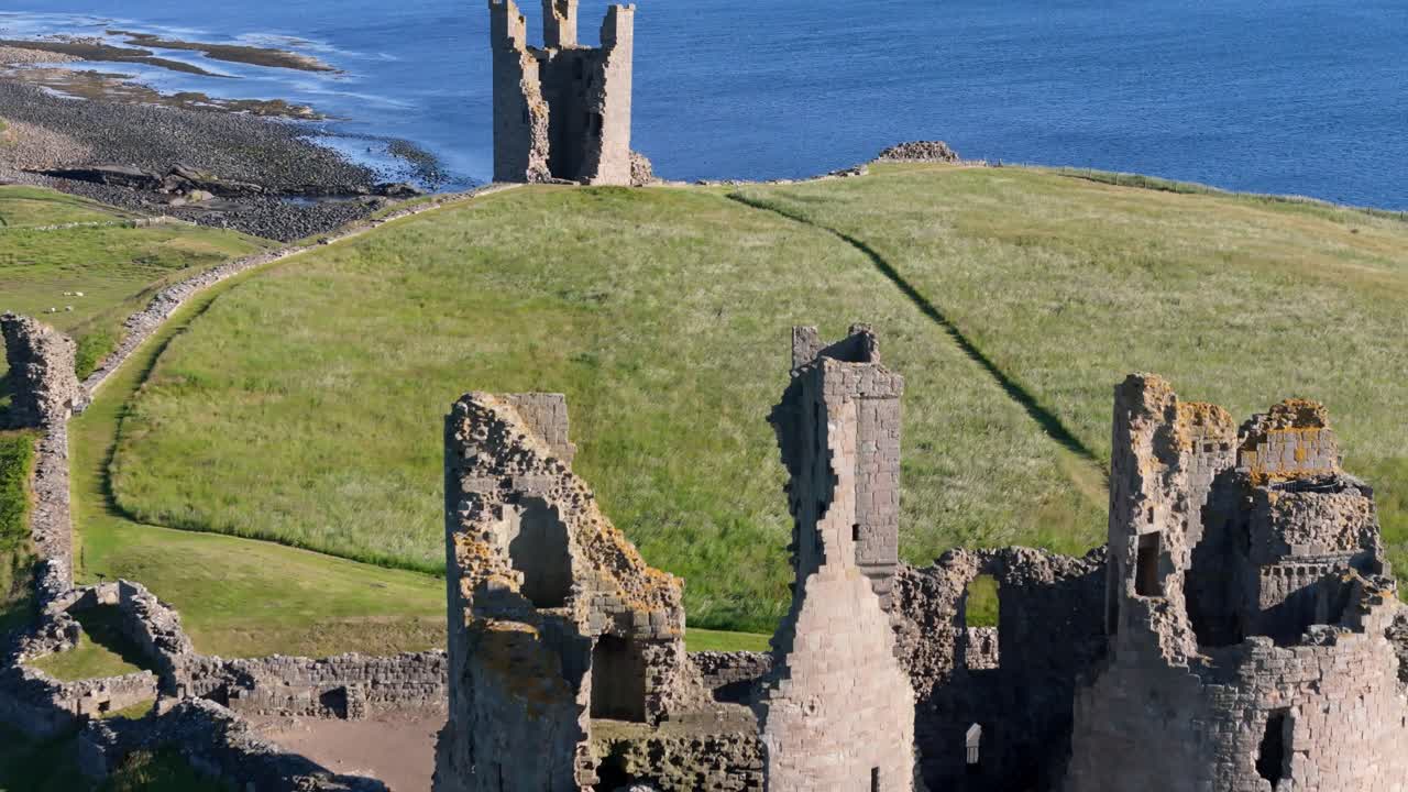 Aerial footage of Dunstanburugh castle ruins on a summer morning with no people