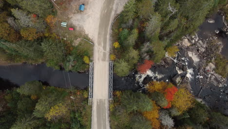 top-view-down-aerial-footage-of-a-bridge-over-a-fast-flowing-creek-that-plunges-into-a-basin-with-a-waterfall-just-behind-the-crossing