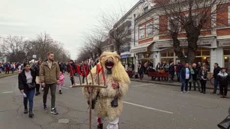 masked and sheepskin coated locals frighten the busó-walking festival visitors with pitchforks on the main street of mohacs during the day in hungary.