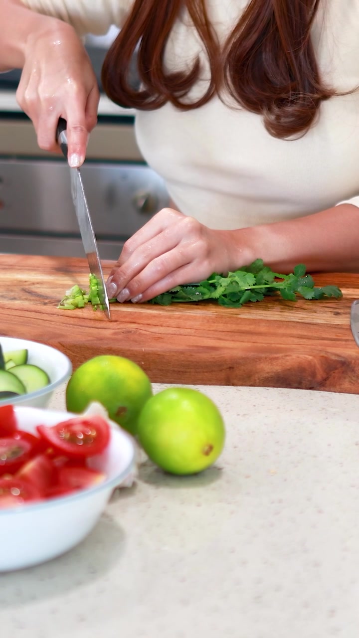 Una persona trita abilmente il coriandolo su un tagliere di legno, circondata da ingredienti freschi in una cucina luminosa.