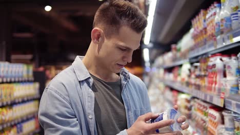 Young-man-chooses-yogurt-or-sour-cream-in-the-supermarket,-customer-selects-product-on-the-milk-products-shelves-in-the-store