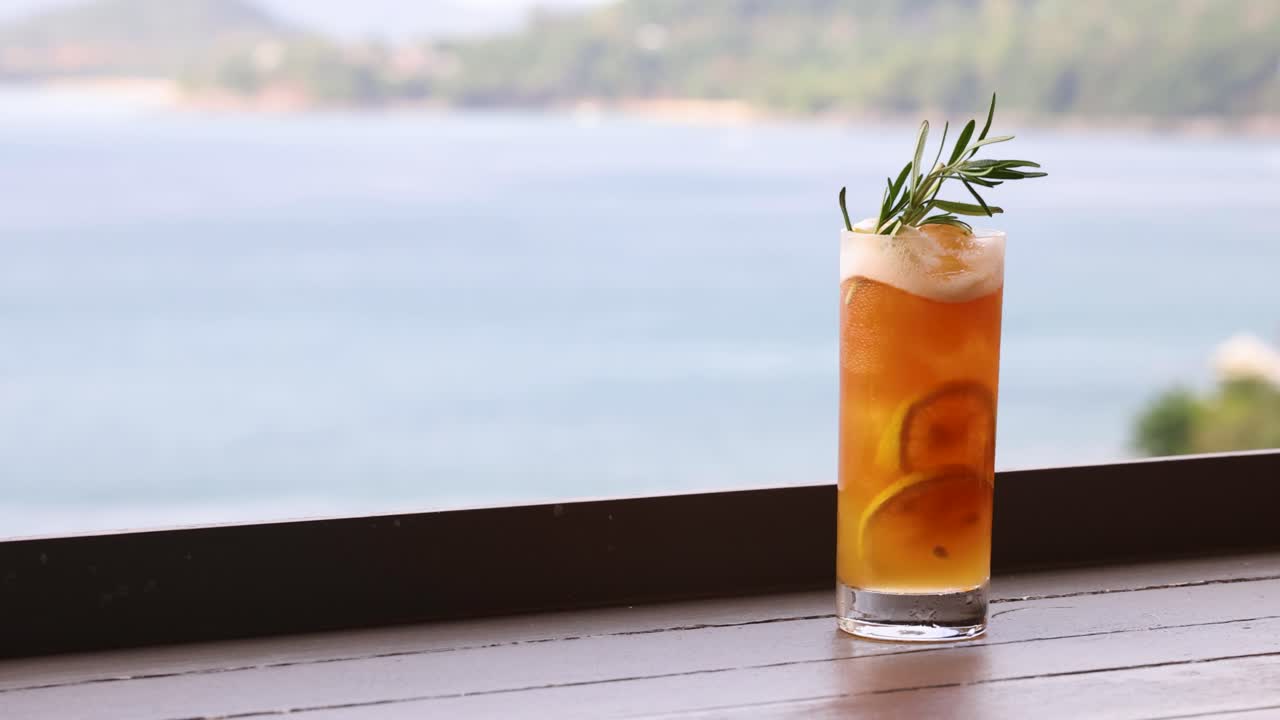 한 손이 바가 테이블에서 테일을 꺼내서 아름다운 바다 배경으로 다른 술을 남니다.