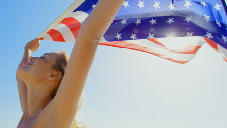 Side-view-of-young-Caucasian-woman-holding-a-American-flag-on-the-beach-4k