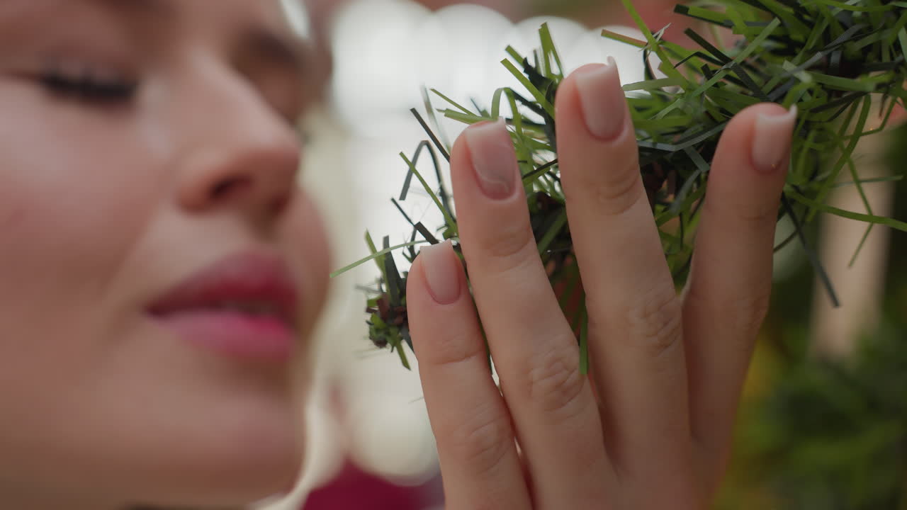 Close-up of white lady affectionately holding Christmas tree while smelling it, background features soft bokeh light effect, with unclear figure moving
