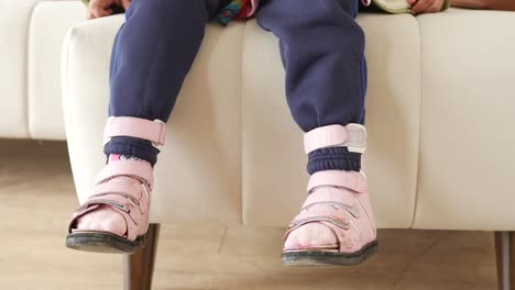 a child wearing pink orthopedic shoes is sitting on a couch