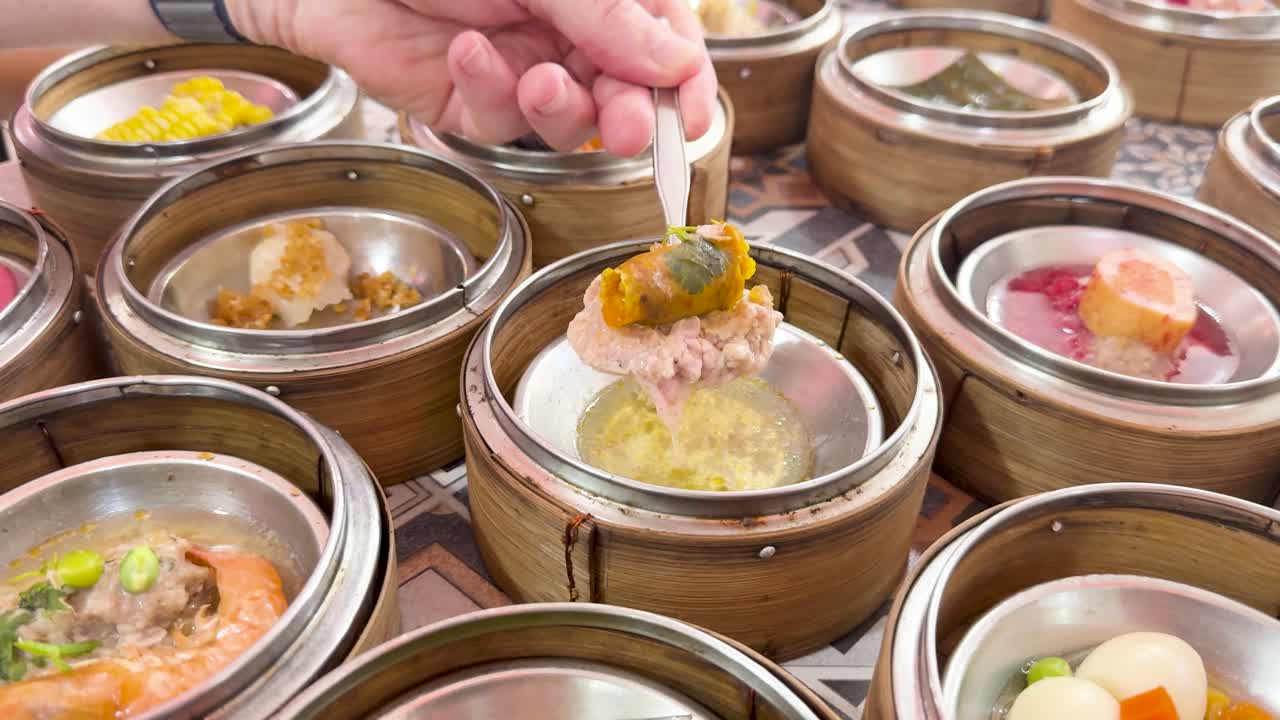 Hand uses fork to pick up dim sum from bamboo basket amid assorted steamed dishes