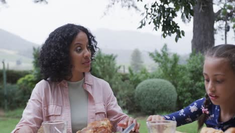 happy biracial parents and daughter eating meal at dinner table in garden, slow motion