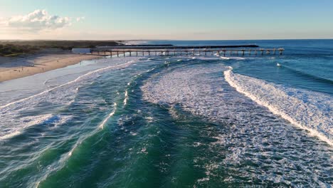 drone captures sweeping views of gold coast's broadbeach, highlighting waves and jetty under warm sunset lighting