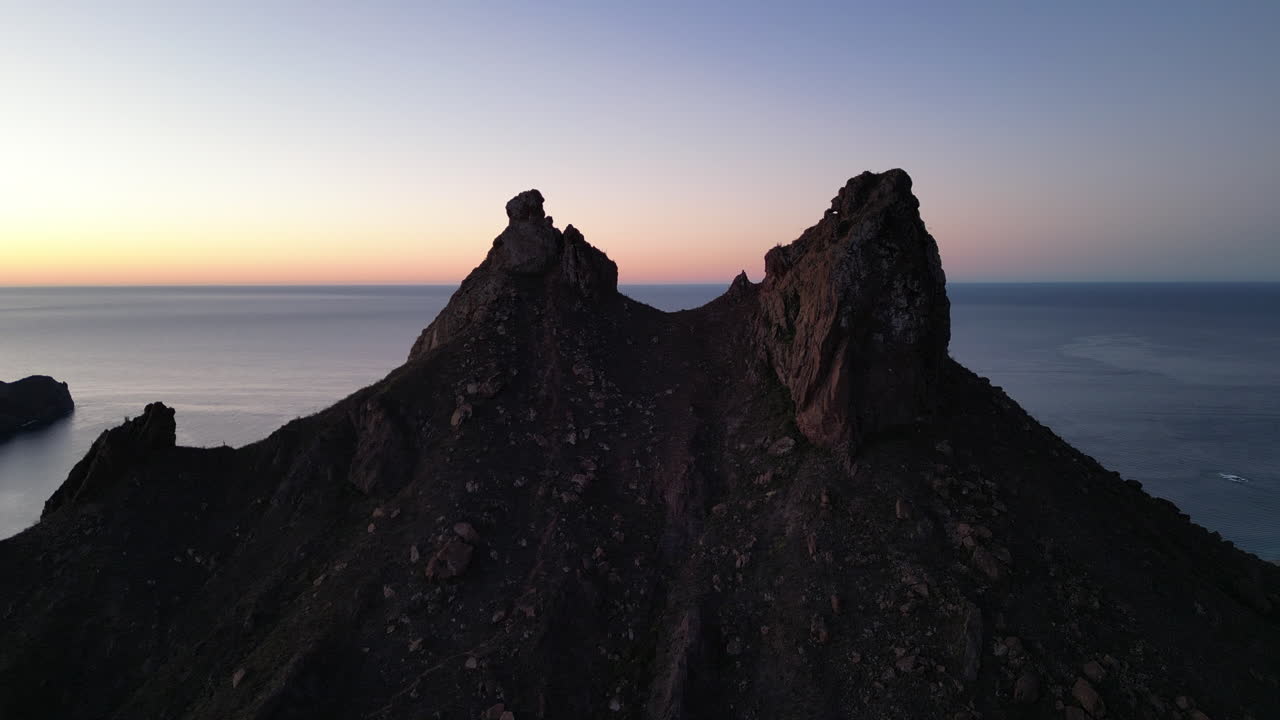 Aerial shot of a mountain with two peaks at sunrise with the sea in the background
