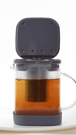 una corriente de agua caliente que se vierte en un infusor de té dentro de una taza de vidrio con un fondo oscuro