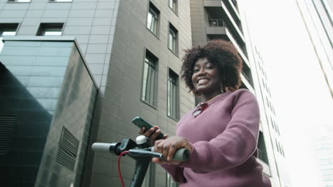 portrait of young african american woman with e-scooter and smartphone in city