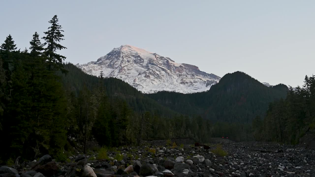 Aerial drone shot of Mount Rainier rising above alpine forest and riverbed in the Pacific Northwest wilderness