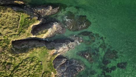 Coastal-Cliff-Waters-Along-the-Cornish-Coastline,-Aerial-Top-Down-Spiraling-Drone-Descending-Over-the-Land-and-Sea,-UK