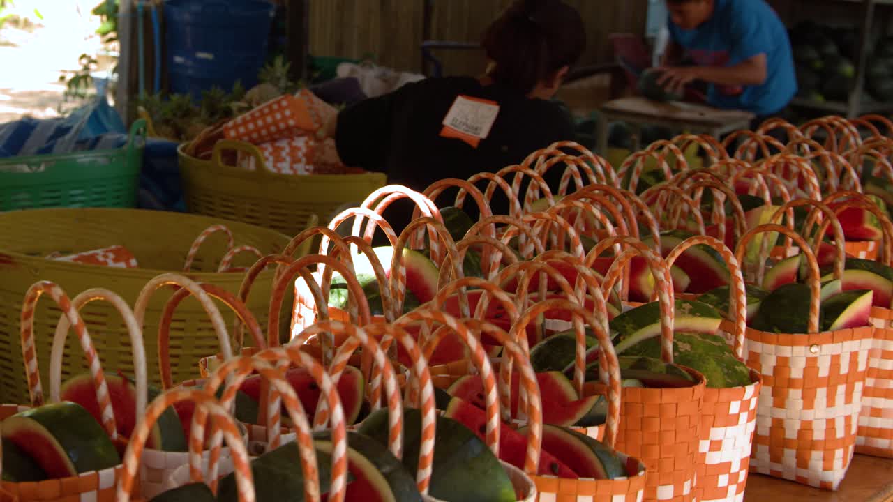 晴れた屋外のタイの市場の屋台に並べられた、オレンジ色のカゴに入ったスライススイカの列