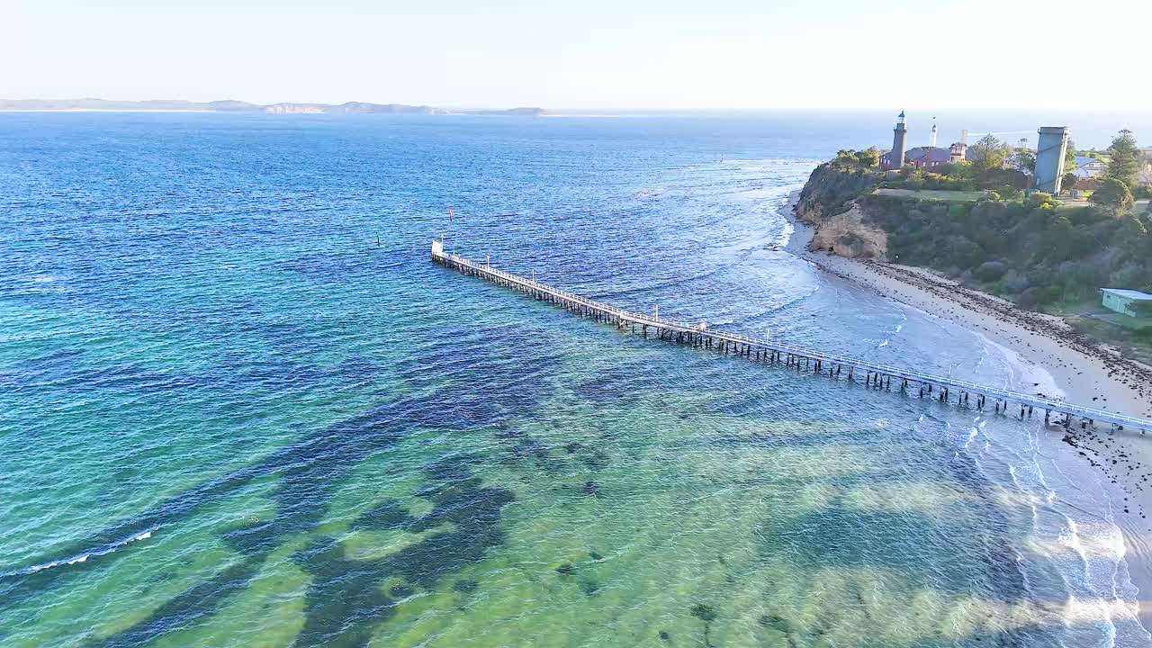 Drone footage captures the serene coastline of Bellarine Peninsula, highlighting a long pier extending into the vibrant blue sea