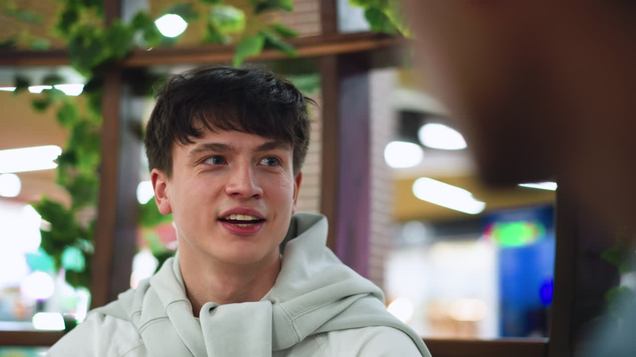 European guy smiling while friend deeply engaged in conversation, indoor casual setting with subtle background blur, warm expression showing connection and attentiveness in relaxed social interaction
