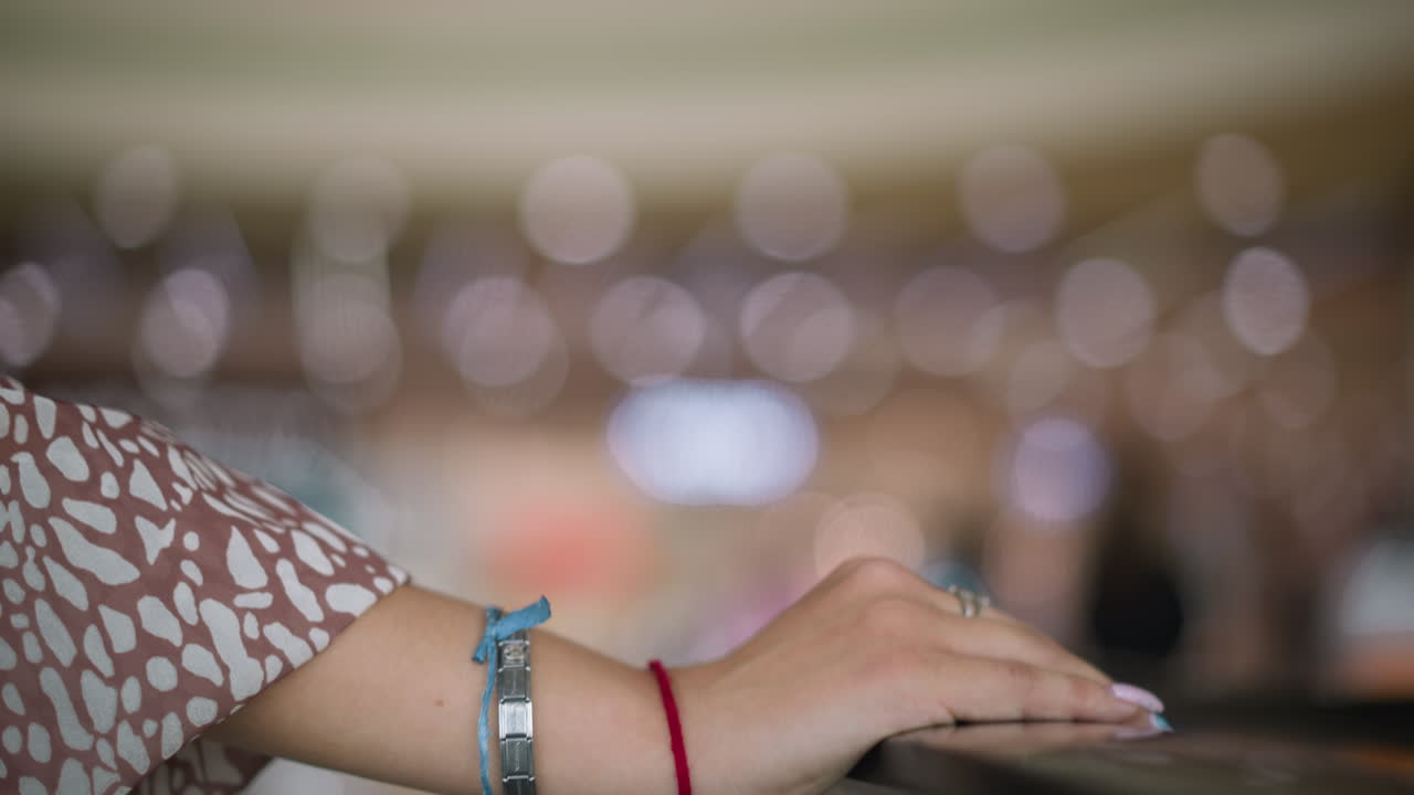 primer plano de una mano individual descansando en una barandilla de hierro, adornada con un brazalete de cadena, cuerdas rojas y azules en la muñeca, contra luces bokeh suaves en el fondo