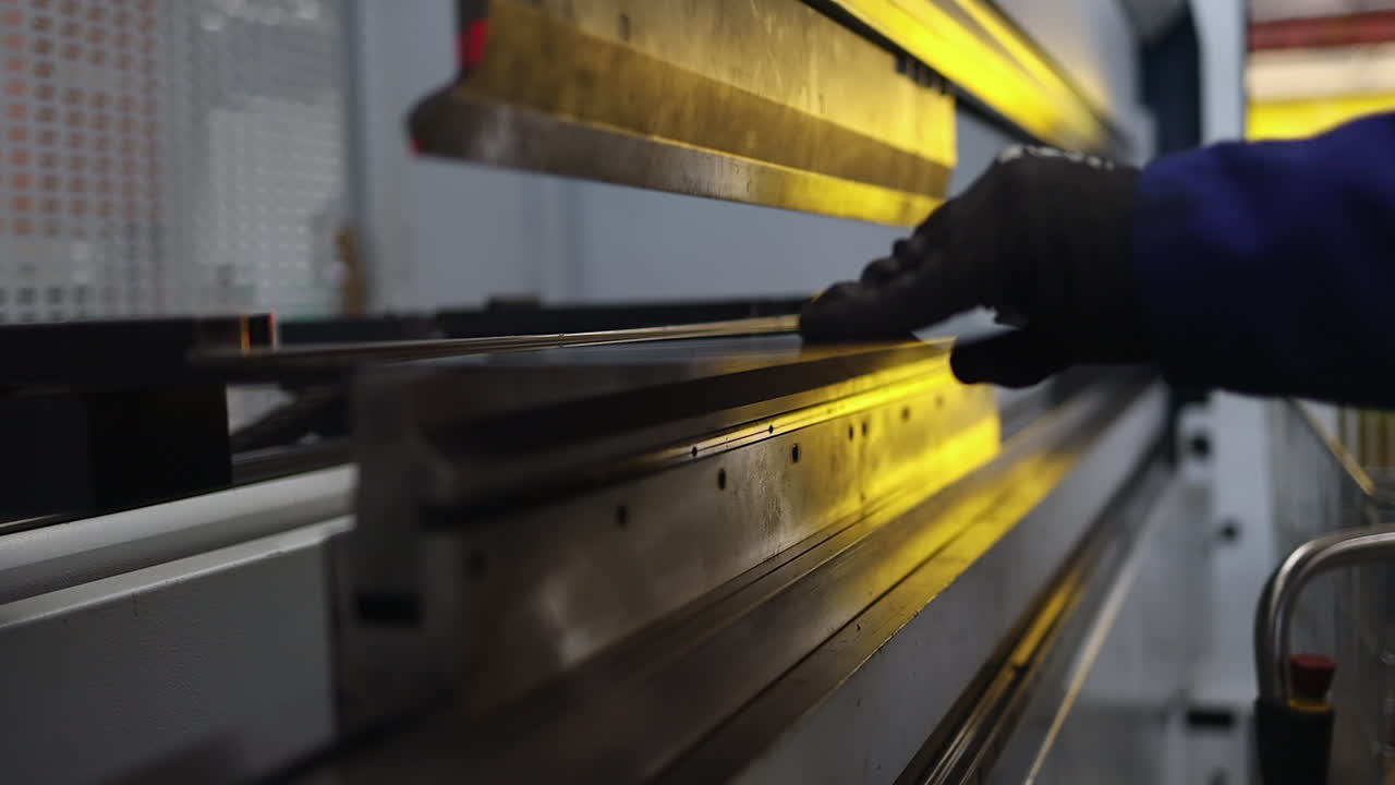 Fabrication worker loads sheet steel into bending machine, gold light