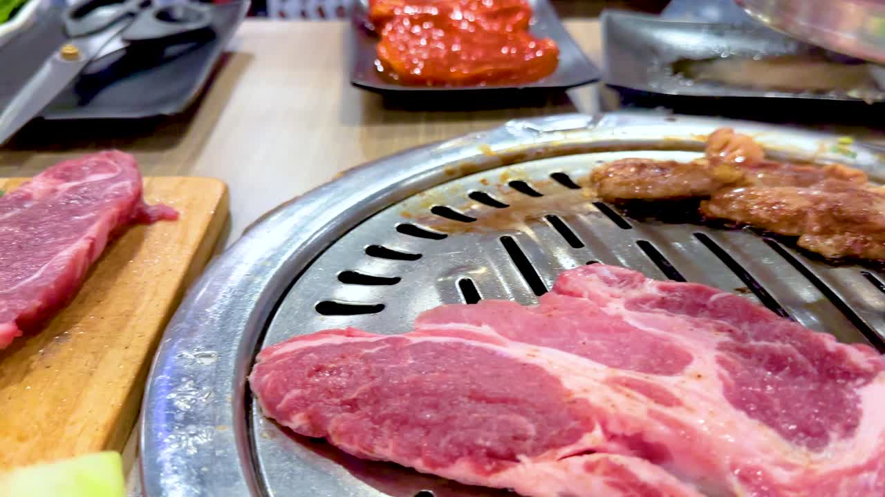 Sizzling meat on a grill with fresh lettuce in a vibrant Bangkok setting. Bright lighting enhances the lively dining atmosphere