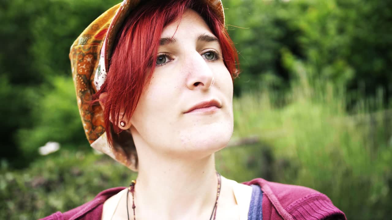 느린 동작으로 배경에 녹색 공원이 있는 의료용 분홍색 얼굴 마스크를 벗고 있는 어린 빨간 머리 소녀