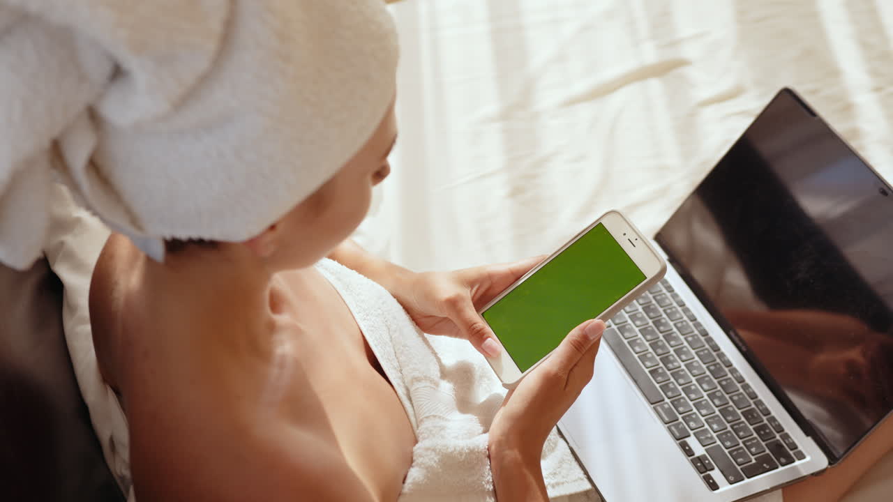 Donna che lavora al laptop e al telefono a letto