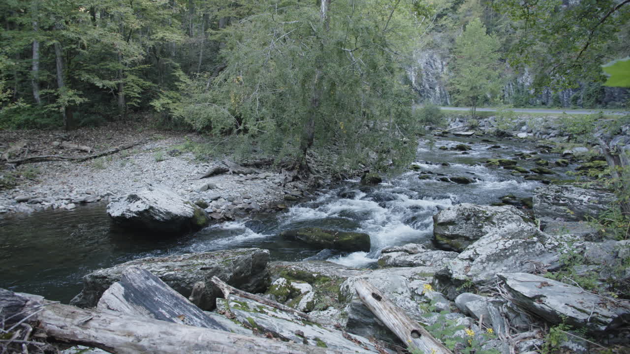 Wide slow motion footage of a creek with water flowing over rocks
